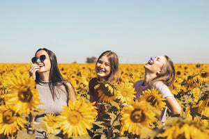 Friends sitting in a field of flowers on a sunny day wearing NÖZ Sunscreen on their face and noses 